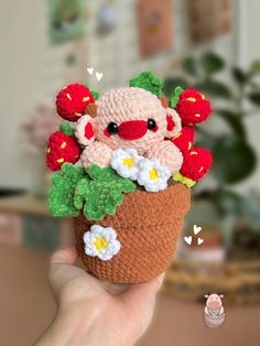 a hand holding up a small crocheted stuffed animal in a pot with flowers