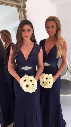 two beautiful women standing next to each other in front of a mirror wearing dresses and holding bouquets