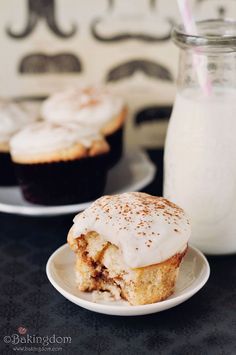 there is a cupcake with icing on the plate next to a glass of milk