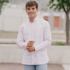 a young man standing in front of a tree smiling at the camera with his hands folded