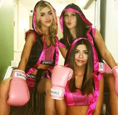 three women in pink boxing gear posing for the camera with gloves on their feet and one woman sitting down