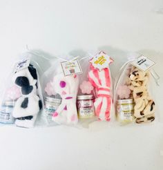 four small stuffed animals in plastic bags on a white surface, one is pink and the other is black