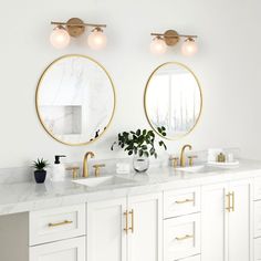 two round mirrors on the wall above double sinks in a white bathroom with gold trim