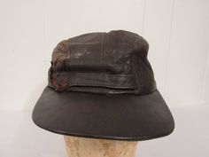 "Vintage 1950s hat. Made of brown leather. Has a corduroy flip down ear cover and quilted lining. Made by the denim jeans company LEE. Label reads: LEE GENUINE LEATHER. Hat is about a size medium(7) with the ear flap down and is a size small(6 7/8) with the flap up inside. Hat is in good condition. Has some leather surface breaks and some paint. Inside 5\" of lining at front sweatband is deteriorated." Military Style Brown Baseball Cap, Vintage Winter Baseball Cap With Short Brim, Vintage Leather Hats For Winter, Vintage Leather Winter Hats, Military Style Brown Flat Cap, Brown Military Flat Cap, Brown Military Style Flat Cap, Retro Leather Cap, Military Style Brown Hat With Curved Brim