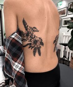 the back of a woman's body with flowers tattooed on her left shoulder and chest