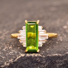 an emerald and diamond ring sitting on top of a rock