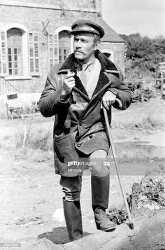 an old man with a cane and hat standing in front of a house, holding a cane