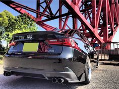 the rear end of a black car parked in front of a red bridge