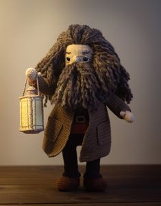 a crocheted doll holding a basket and wearing a long coat, standing on a wooden table