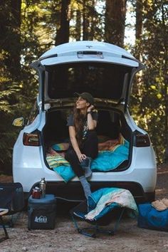 a woman sitting in the back of a van with her camping gear