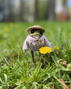 a small stuffed animal sitting in the grass with a dandelion