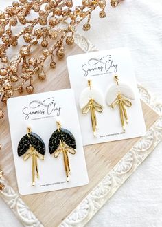 two pairs of earrings with black and white designs on them sitting on a wooden tray