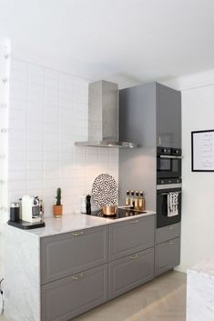 a kitchen with gray cabinets and marble counter tops, white tile backsplash and gold accents