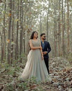 a man and woman standing in the middle of a forest with leaves on the ground