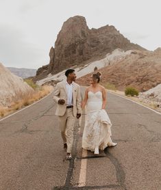 a bride and groom walking down the road in front of some mountain formations at their wedding