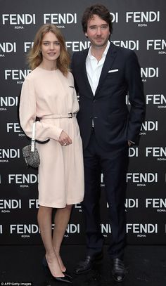 a man and woman standing next to each other in front of a black wall with the words fendi on it