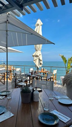 an outdoor dining area overlooking the ocean with umbrellas and tables set up for two