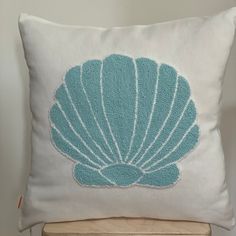 a blue and white pillow with an embroidered shell design on it sitting on a wooden chair