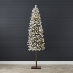 a white christmas tree with snow on it in front of a black wall and wooden floor