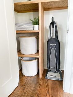 a vacuum cleaner is on the floor next to a shelf with towels and other items