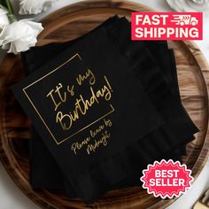 two black napkins with gold foil lettering on them sitting on top of a wooden plate