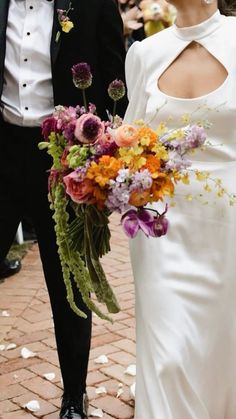 the bride and groom are walking down the street together with flowers in their bouquets