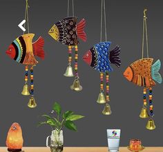 three colorful fish hanging from the ceiling next to a potted plant and glass vase