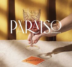 a person holding a wine glass with the word paraiso in front of them on a table