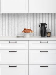 a kitchen with white cabinets and black vases on the countertop, along with a plate of food