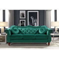 a green couch in a living room with pictures on the wall and two lamps next to it