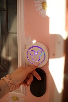 a person is pressing the button on a light switch in front of a pink wall with daisies