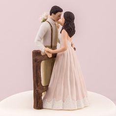 a figurine of a bride and groom kissing in front of a wooden fence