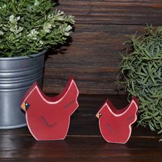 two red birds sitting on top of a wooden table next to a potted plant