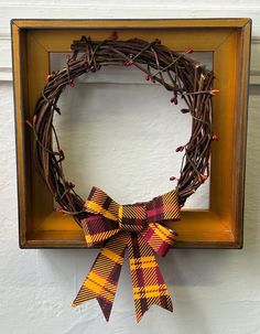 a wreath is hanging on the wall next to a wooden frame with a plaid bow