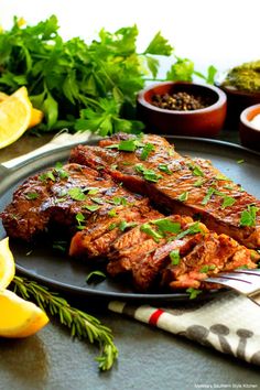 two pieces of steak on a plate with lemons and parsley