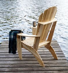 a wooden chair sitting on top of a wooden dock next to the water with a blanket draped over it