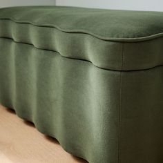 a close up of a green bench cushion on a wooden floor with white walls in the background