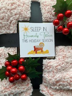 a crocheted christmas blanket with holly leaves and red berries on it, next to a sign that says sleep in heavenly peace this holiday season