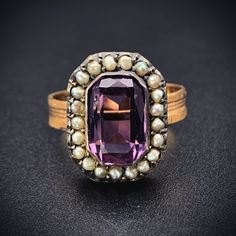 "Amethyst stones have been thought for generations to provide protection and were worn by the Ancients as a talisman for luck. The beautiful violet purple hue has also had an allure not to be resisted. Beloved by Victorians as well, it was the first color a widow was allowed to wear after coming out of mourning.  This ring was converted from an antique brooch. The beautiful, faceted rectangular amethyst is haloed by 21 natural seed pearls, which the Victorian jewelers implemented to represent \"tears of sorrow\". The faceted emerald cut amethyst stone is paired with a replica textured band, giving its new incarnation as a ring is a lovely way to showcase this classic combination of amethyst and pearl.   Details (approximate) Size: 7 Weight:  5 grams Materials: Gold, Amethyst, Seed Pearl Me Heirloom Multi-stone Amethyst Ring, Heirloom Multi-stone Purple Amethyst Ring, Fine Jewelry Purple Amethyst Multi-stone Ring, Purple Multi-stone Amethyst Ring Fine Jewelry, Purple Multi-stone Amethyst Ring In Fine Jewelry Style, Purple Multi-stone Amethyst Ring, Formal Purple Multi-stone Amethyst Ring, Multi-stone Purple Gemstone Ring, Purple Multi-stone Gemstone Rings