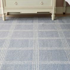 a blue carpet in a bedroom with a white dresser and bed behind the rugs