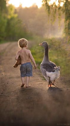 a young boy walking down a dirt road next to a duck