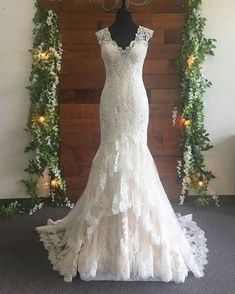 a wedding dress is displayed on a mannequin in front of a wall with greenery