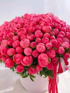 a large bouquet of pink tulips in a white vase with a red ribbon