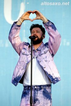 a man making a heart with his hands while standing in front of a microphone on stage