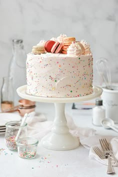 a white cake with sprinkles and cookies on top sitting on a table