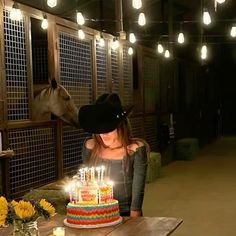 a woman blowing out candles on a birthday cake with a horse in the back ground