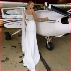 a woman in a white dress standing next to an airplane