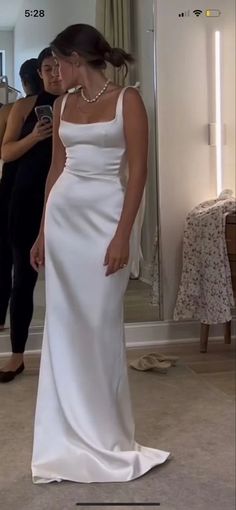 a woman standing in front of a mirror wearing a white dress