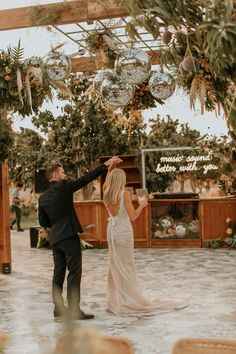 a bride and groom dancing together in an outdoor wedding venue with greenery hanging from the ceiling