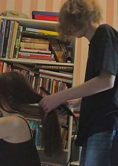 two people standing in front of a bookshelf and one person cutting another persons hair